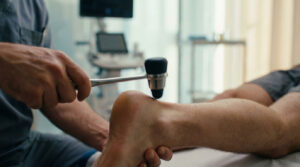 A healthcare professional uses a reflex hammer on a patient's foot in a clinical setting.