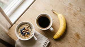 A bowl of oatmeal topped with blueberries and almonds, a cup of black coffee, and a banana on a wooden table.