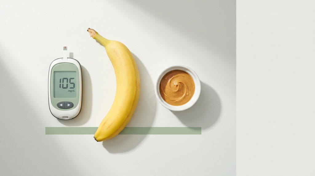 A glucose meter shows 105 mg/dL next to a banana and a bowl of peanut butter on a light surface.