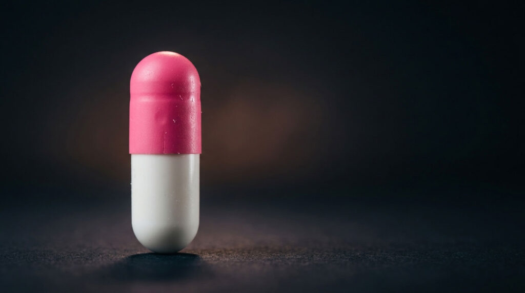 A pink and white capsule stands upright on a dark surface with soft lighting highlighting its features.