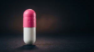 A pink and white capsule stands upright on a dark surface with soft lighting highlighting its features.