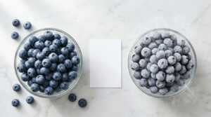 Two glass bowls filled with fresh and frozen blueberries on a marble surface with a blank card in between.