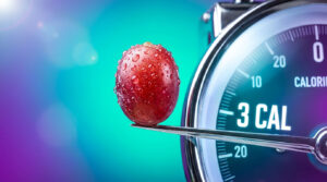 A close-up of a red grape on a spoon with a calorie gauge showing 3 calories in the background.