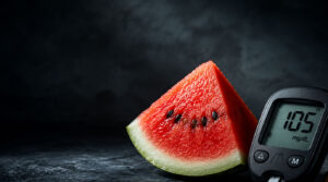A slice of watermelon with black seeds next to a glucose meter displaying 105 mg/dL on a dark background.