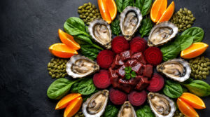 A colorful arrangement of oysters, beets, spinach, oranges, and pumpkin seeds on a dark background.