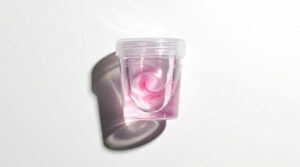 A clear plastic cup filled with pink liquid casts a shadow on a white background.