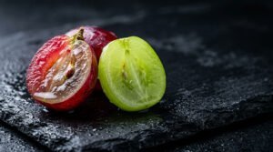A sliced red and green grape on a dark slate surface with droplets of water.