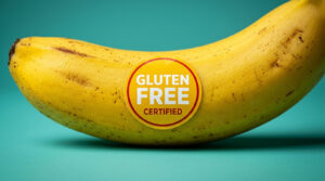 A ripe yellow banana with a gluten-free certified sticker on a teal background.