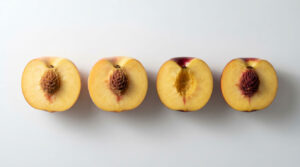 Four halved peaches display their yellow flesh and pits on a white background.