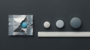 A blue pill is next to three tablets and a ruler on a dark background.