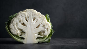 A fresh cauliflower cut in half, showcasing its intricate florets and green leaves against a dark background.