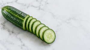 A fresh cucumber sliced into thin rounds on a marble surface. Water droplets are visible on the cucumber skin.