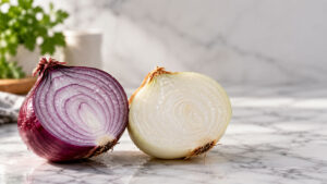 A halved red onion and white onion sit on a marble countertop with fresh herbs in the background.