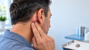Man touches his ear in a medical setting with tools nearby.