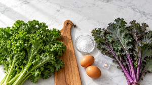 Fresh kale and leafy greens with eggs and salt on a marble surface.