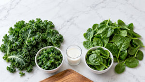 Fresh kale and spinach arranged on a marble surface with a glass of milk and bowls of greens.